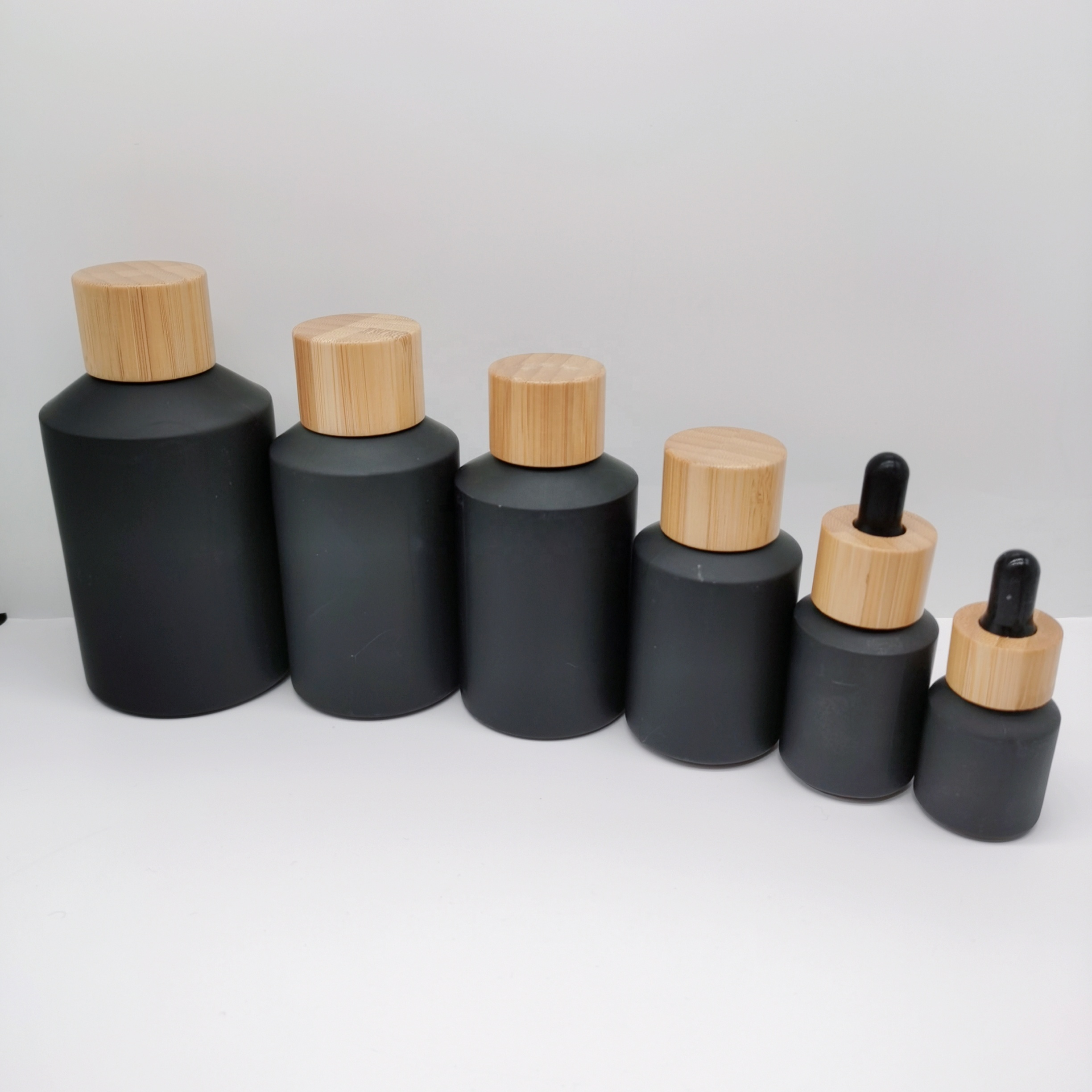 Factory production cosmetic glass bottles packaging slant shoulder matte black glass bottle and jar with bamboo lid series
